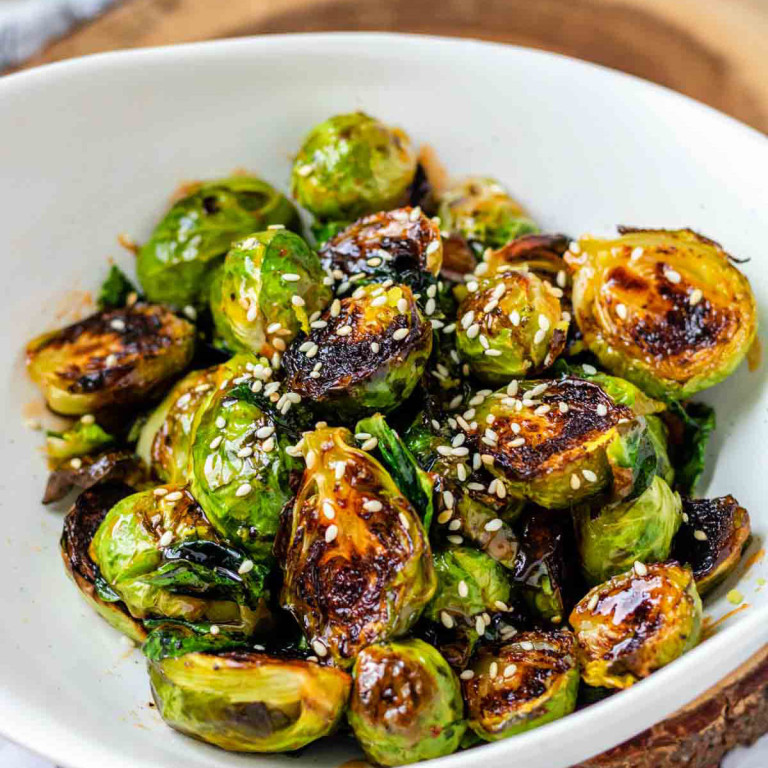 A bowl of roasted Brussels sprouts with sauce and sesame seeds on them.