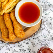 A bowl of honey sriracha sauce beside chicken fingers and fries.