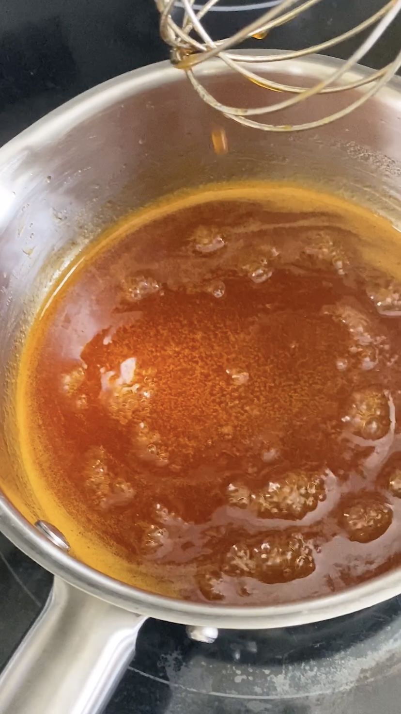 Heated honey sriracha sauce dripping off a whisk back into a saucepan.
