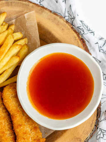 A bowl of honey sriracha sauce beside chicken fingers and fries.