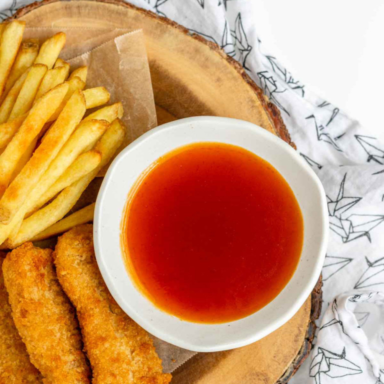 A bowl of honey sriracha sauce beside chicken fingers and fries.