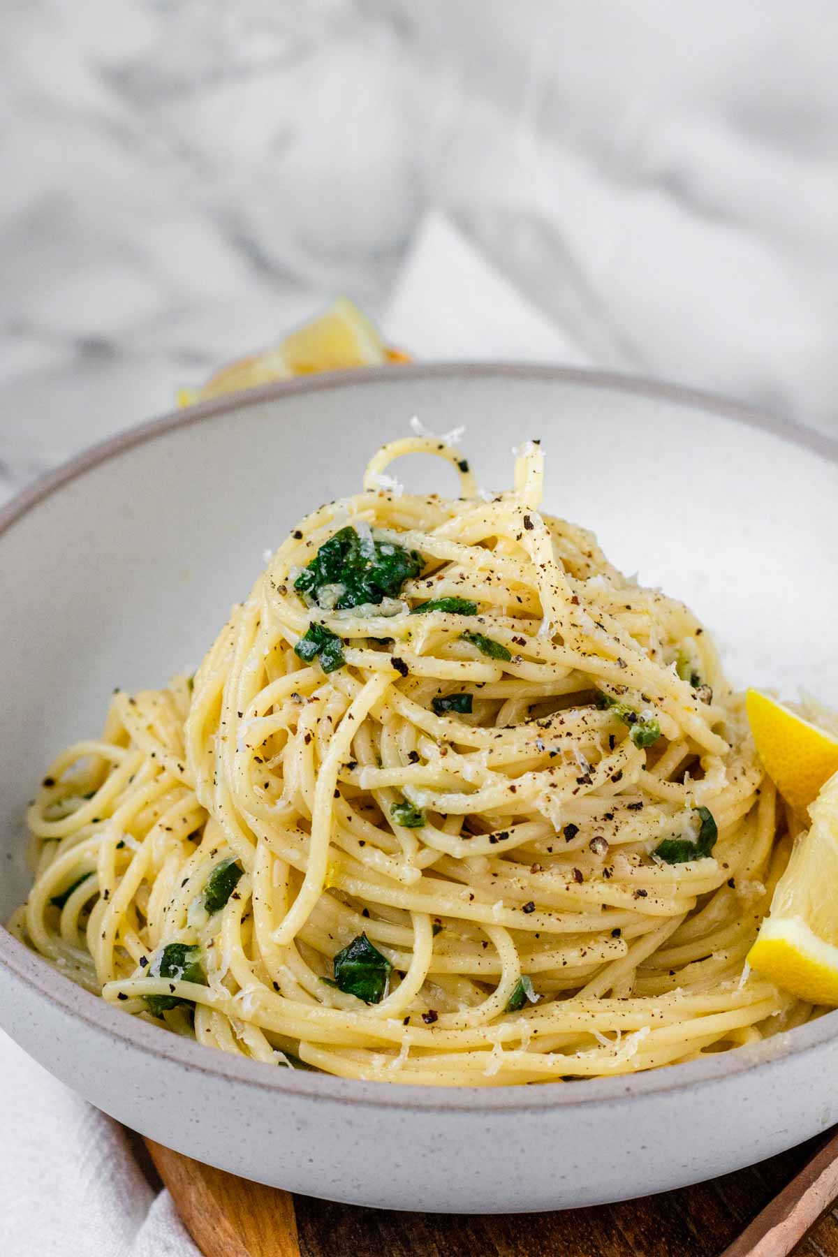 Pasta swirled in a bowl with spinach, cheese, and lemon slices on the side.