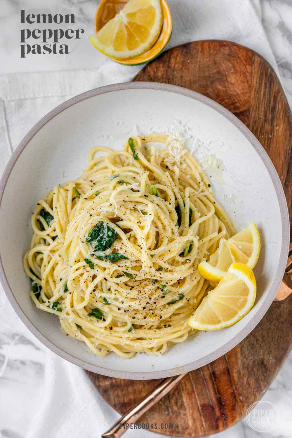 Pasta swirled in a bowl with spinach, cheese, and lemon slices on the side.