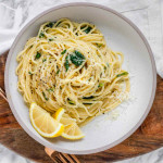 Pasta swirled in a bowl with spinach, cheese, and lemon slices on the side.