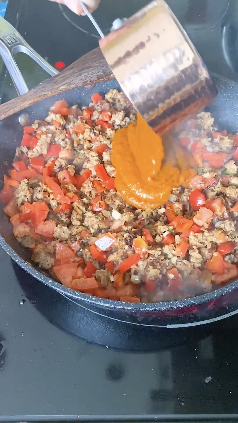 Adding enchilada sauce to a skillet of cooked beyond beef and vegetables.
