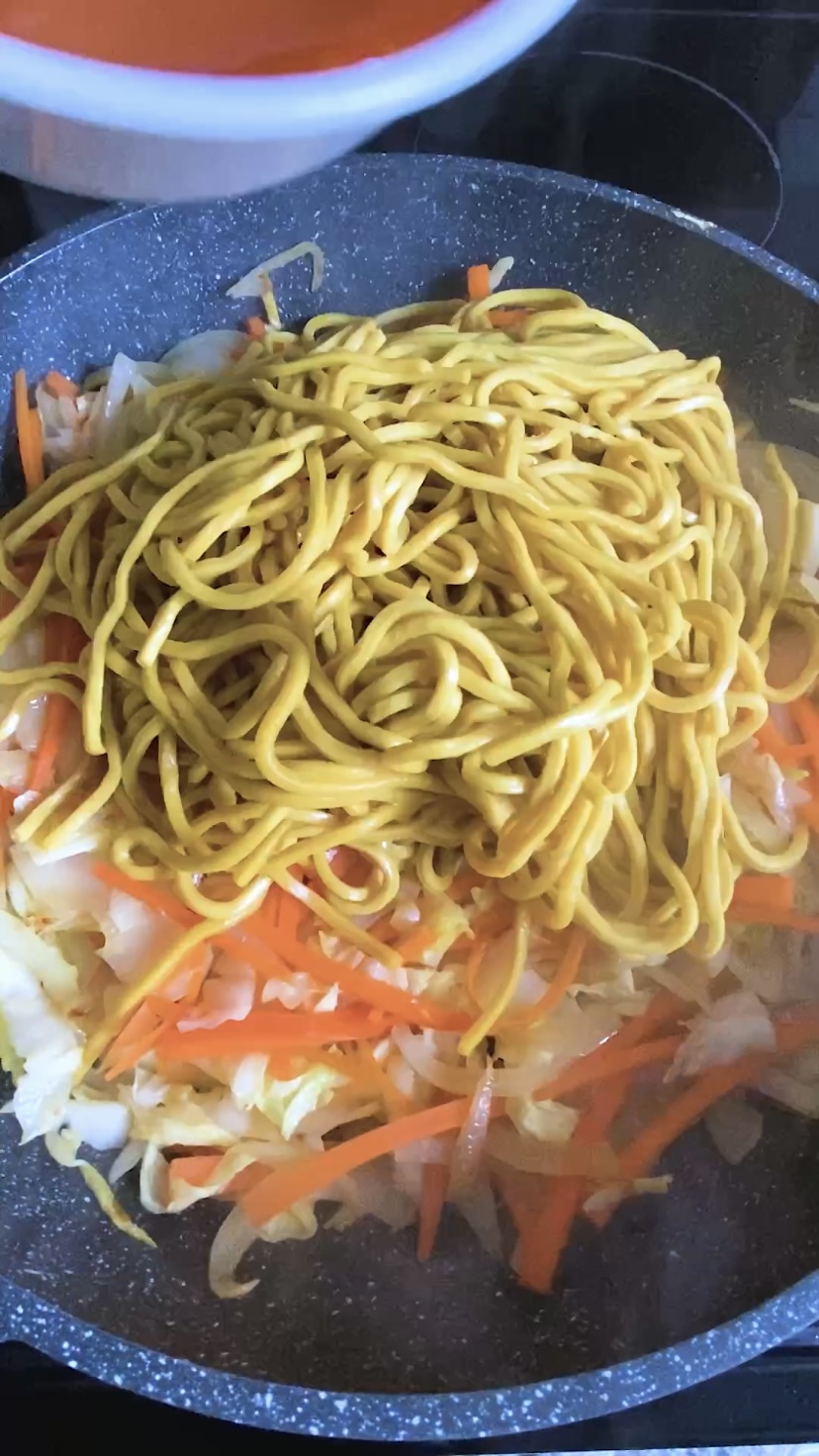 Noodles are added to a skillet of vegetables.