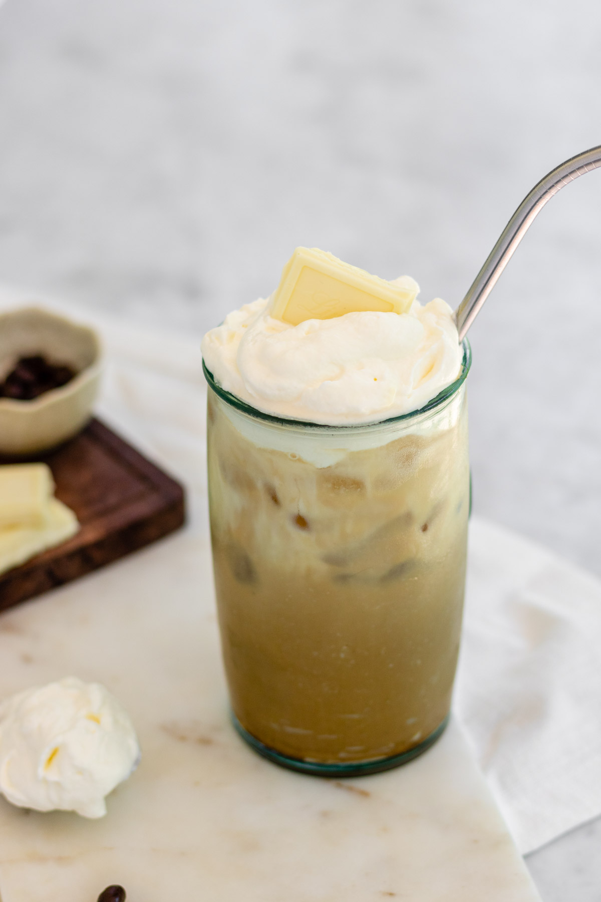Iced coffee in a tall glass with whipped cream and a white chocolate square on top.