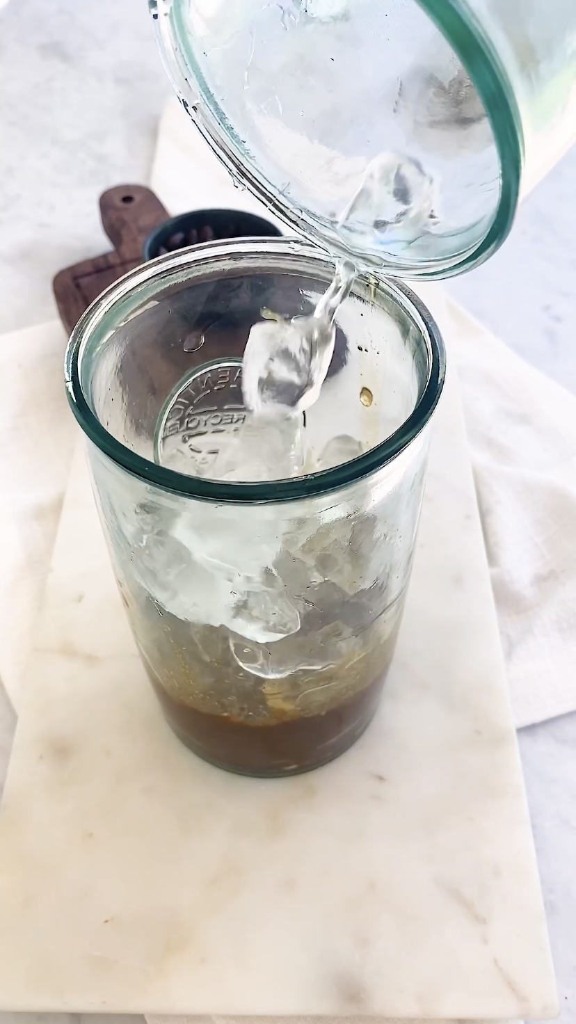 Adding ice to a glass with coffee in the bottom.