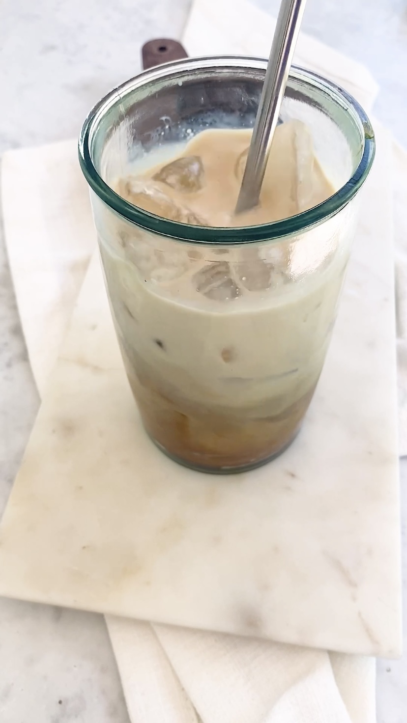 Stirring an iced coffee in a tall glass.