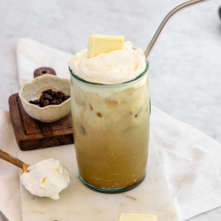 Iced coffee in a tall glass with whipped cream and a white chocolate square on top.