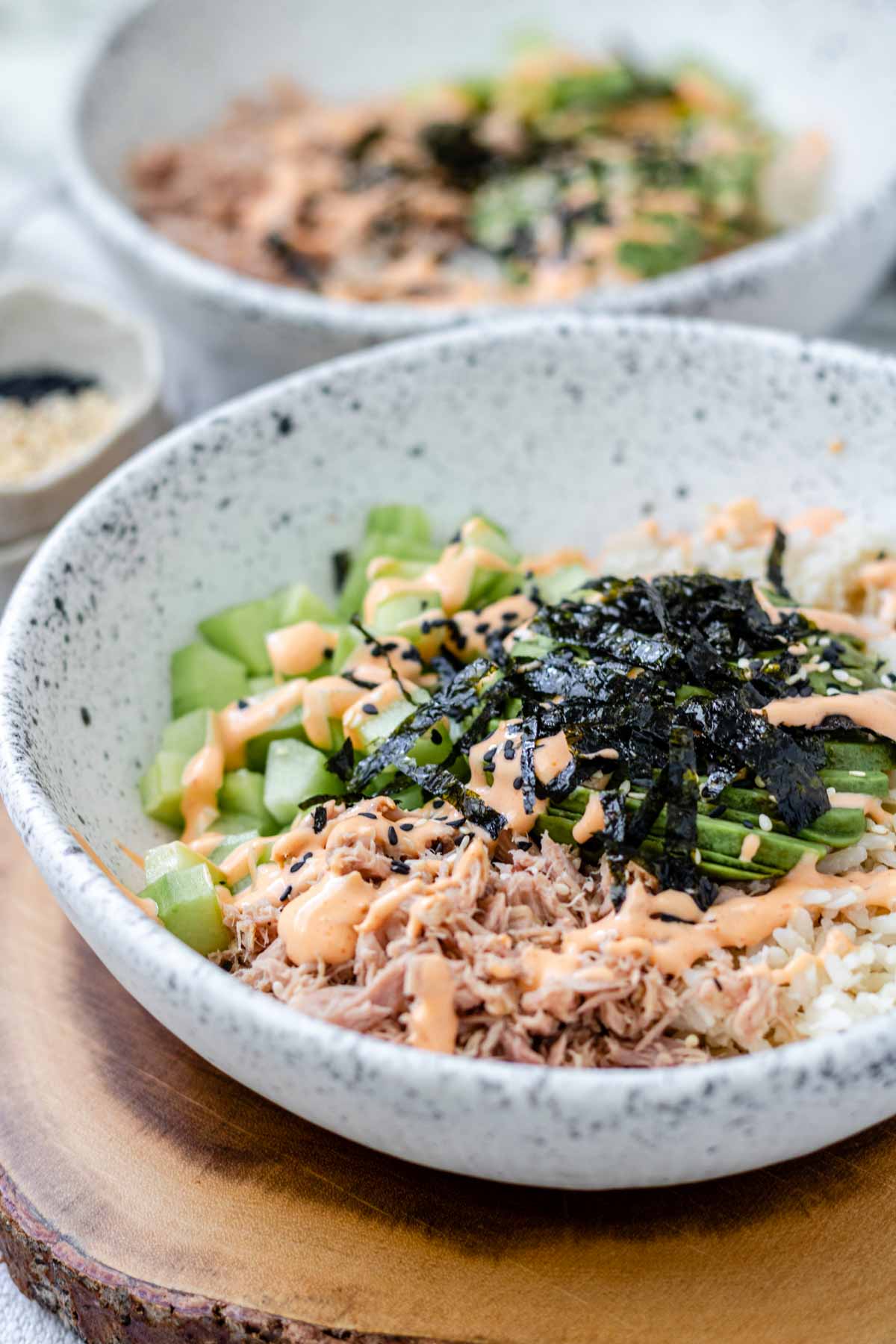 A bowl with rice, tuna, cucumber, avocado, spicy mayo sauce, sesame seeds and flakes of nori.