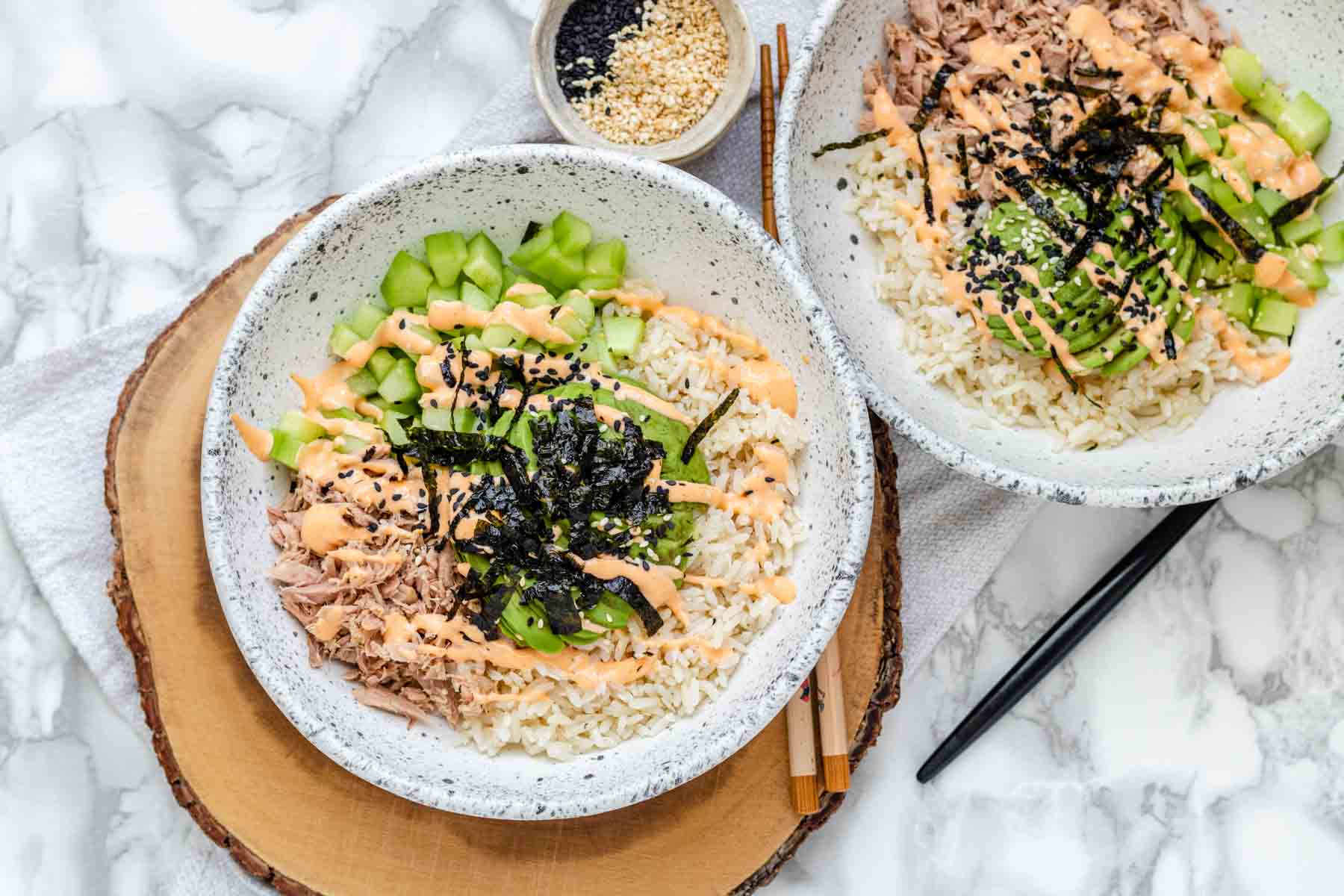 A bowl with rice, tuna, cucumber, avocado, spicy mayo sauce, sesame seeds and flakes of nori.