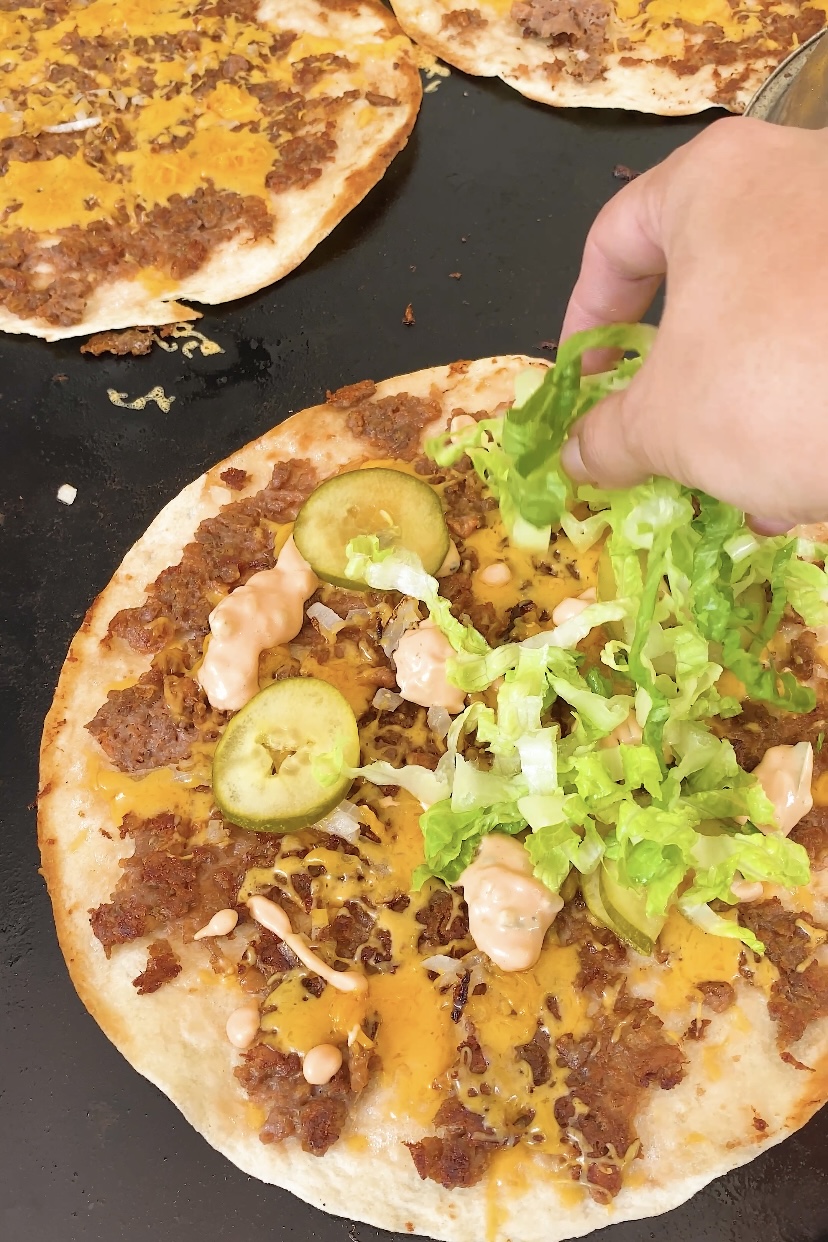 Lettuce and pickle are added to a tortilla with beyond beef and cheese on it.
