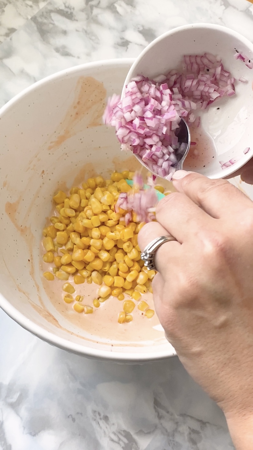 Red onion is added to corn in a bowl.
