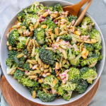 A bowl of broccoli, pepitas, and red onion coated in dressing.