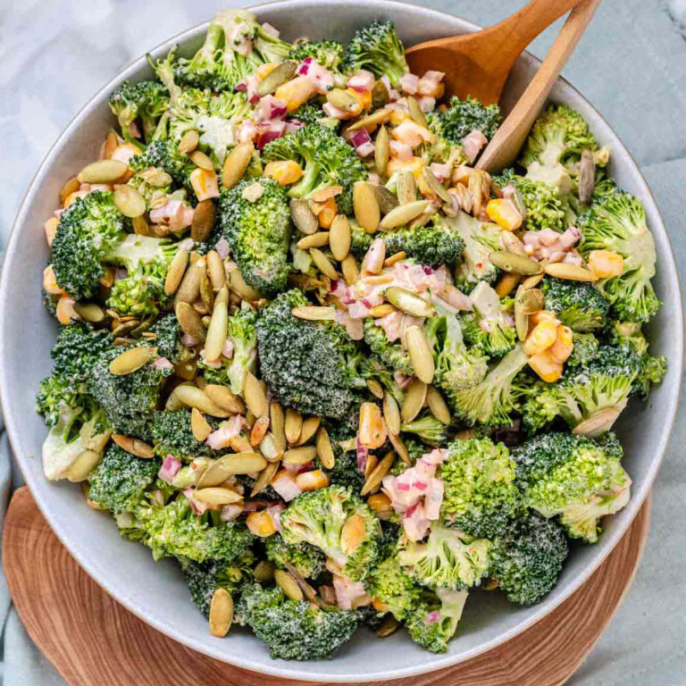 A bowl of broccoli, pepitas, and red onion coated in dressing.