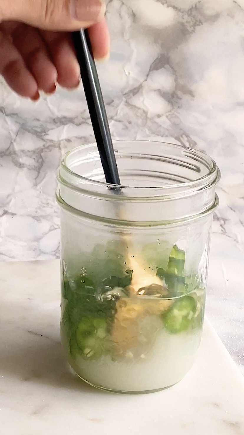 A spoon stir a jar of jalapeno slices, sugar, and water.
