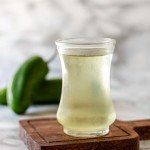 Simple syrup in a small glass jar with jalapenos in the background.