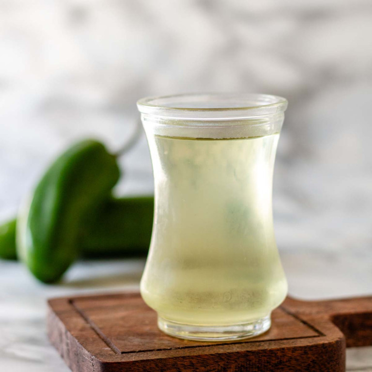 Simple syrup in a small glass jar with jalapenos in the background.