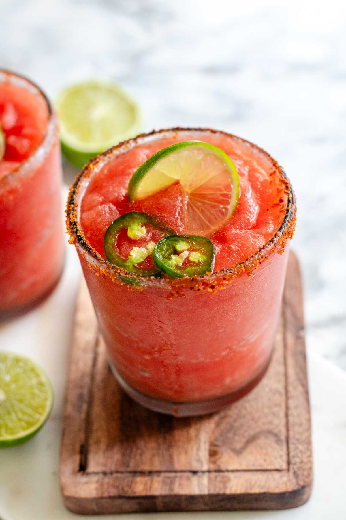 A red margarita in a rimmed glass with jalapeno and lime slices on top.