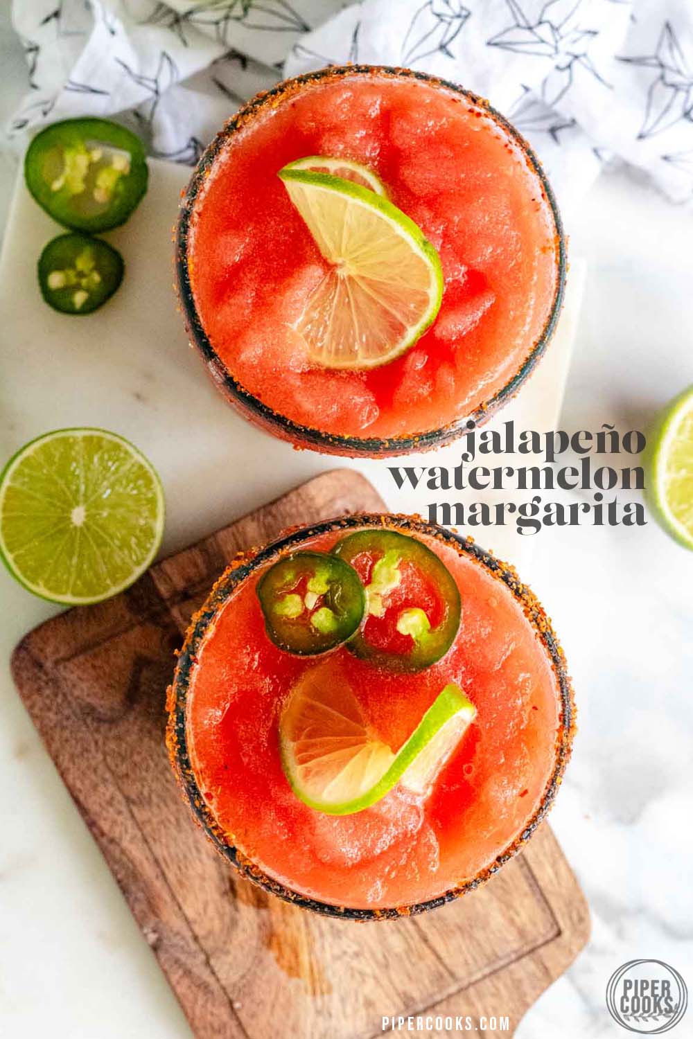 A red margarita in a rimmed glass with jalapeno and lime slices on top with a text title for Pinterest.