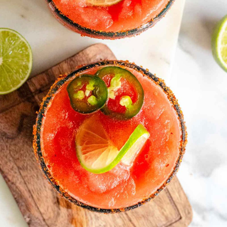 A red margarita in a rimmed glass with jalapeno and lime slices on top.