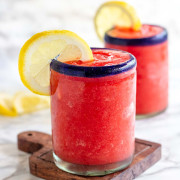 A frozen pink drink in a glass garnished with a lemon slice.
