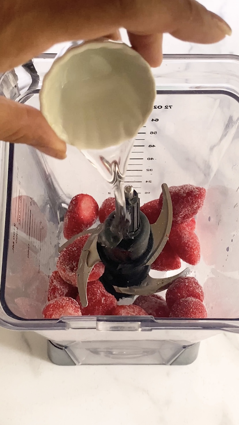Adding simple syrup to a blender of strawberries.