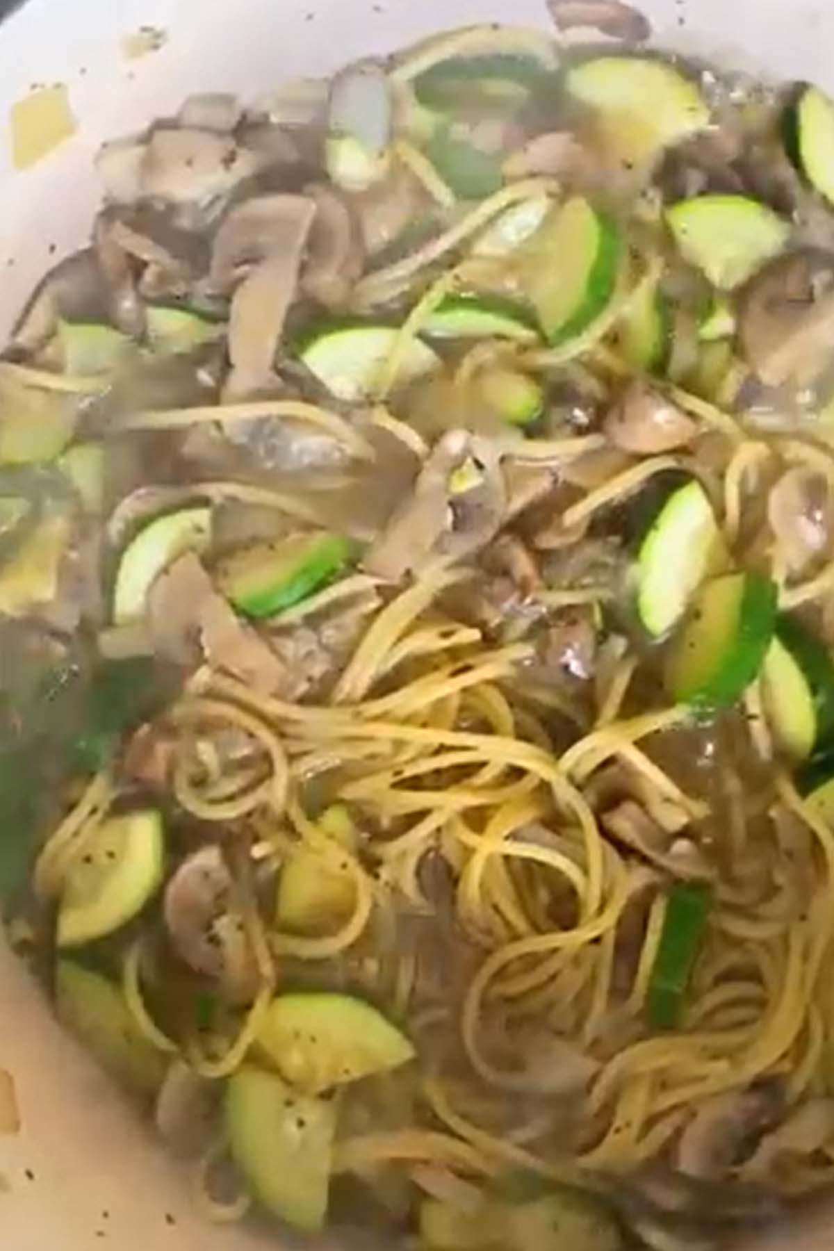 Pasta cooking in water with zucchini and mushrooms.