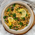 Pasta in a bowl garnished with parsley and lemon slices.