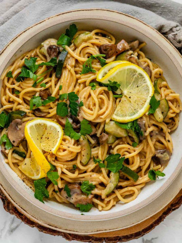 Pasta in a bowl garnished with parsley and lemon slices.