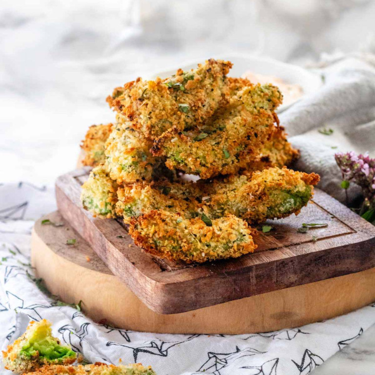 Baked breaded avocado wedges stacked on a wooden board.