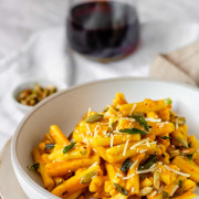 Pasta in a bowl coated in an orange sauce and garnished with sage, cheese, and pumpkin seeds.