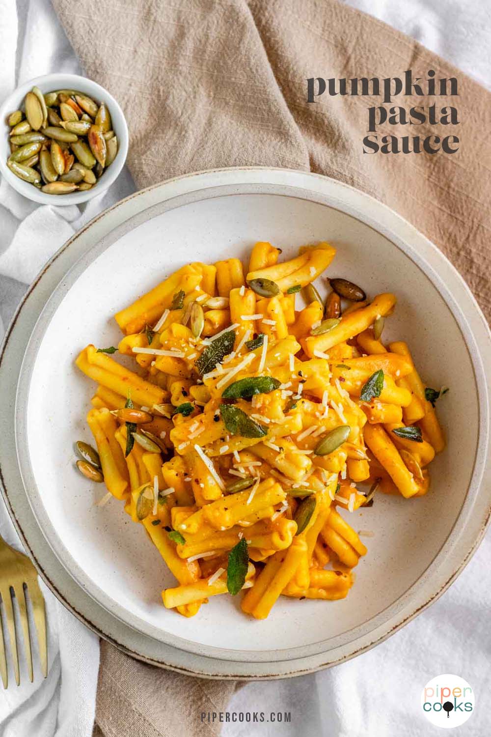 Pasta in a bowl coated in an orange sauce and garnished with sage, cheese, and pumpkin seeds with text for Pinterest.