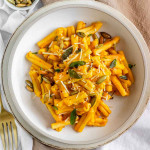 Pasta in a bowl coated in an orange sauce and garnished with sage, cheese, and pumpkin seeds.