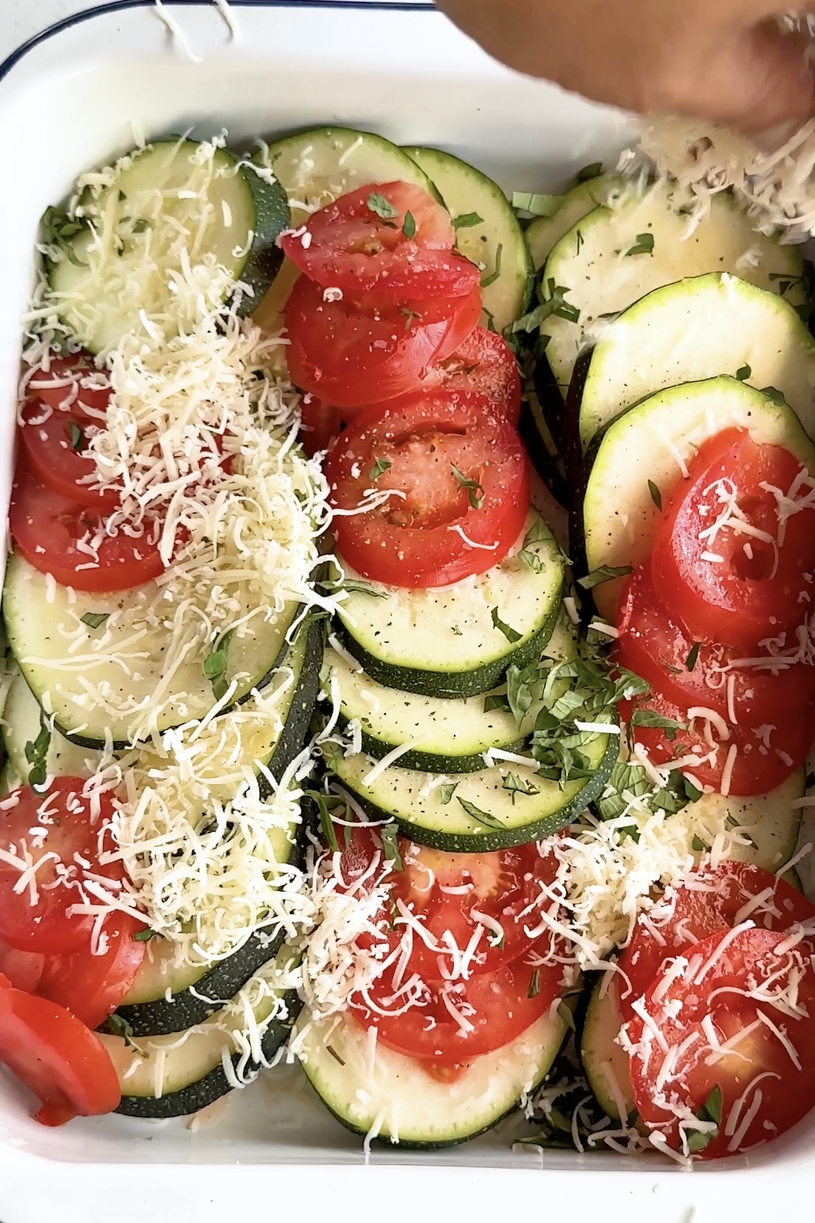 Tomato and zucchini layered in a casserole dish topped with cheese.