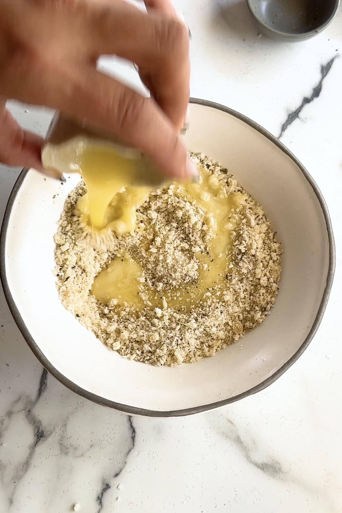 Melted butter is poured into a bowl of bread crumbs.