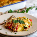 A baked casserole on a plate topped with browned bread crumbs and oregano leaves.