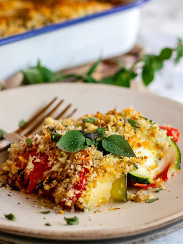 A baked casserole on a plate topped with browned bread crumbs and oregano leaves.