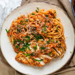 Pasta and chicken on a plate covered in creamy tomato sauce and fresh basil.