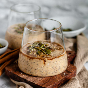 Oats in a glass cup with syrup and pumpkin seeds on top.