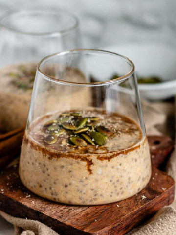 Oats in a glass cup with syrup and pumpkin seeds on top.
