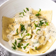Ravioli in a bowl covered in cream sauce with a text title for Pinterest.