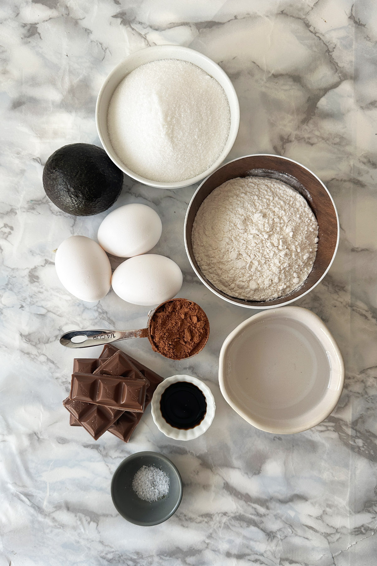 Ingredients for brownies in bowls on a white marble counter.
