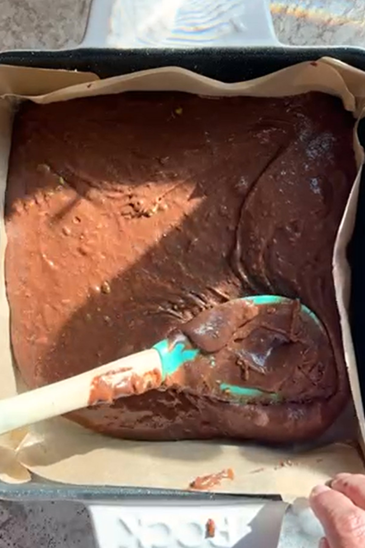 Brownie batter is spread smooth in a baking pan with a spatula.