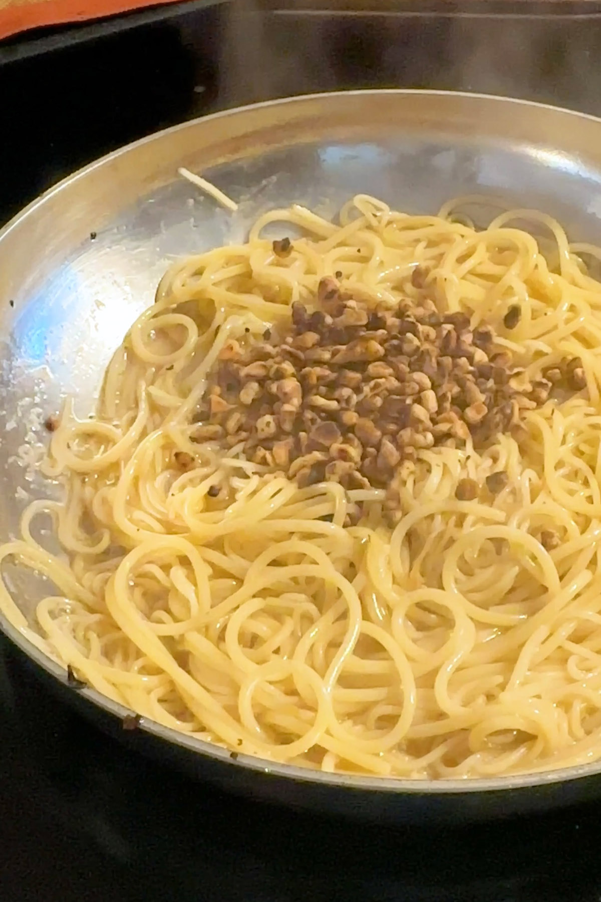 Walnuts are added to pasta in a stainless steel skillet.