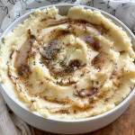 Mashed potatoes in a bowl topped with browned butter and chopped rosemary.