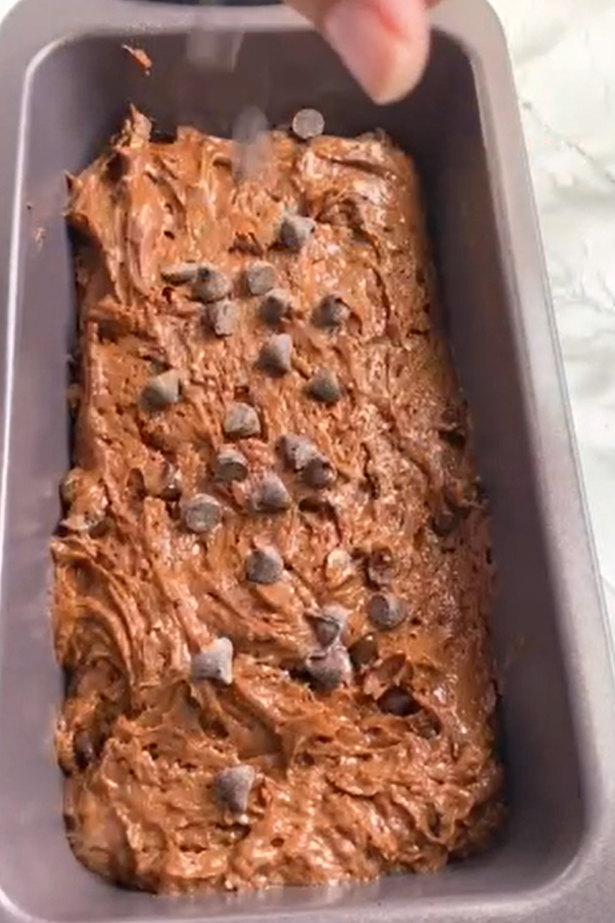 Chocolate chips are added on top of cake batter in a loaf pan.