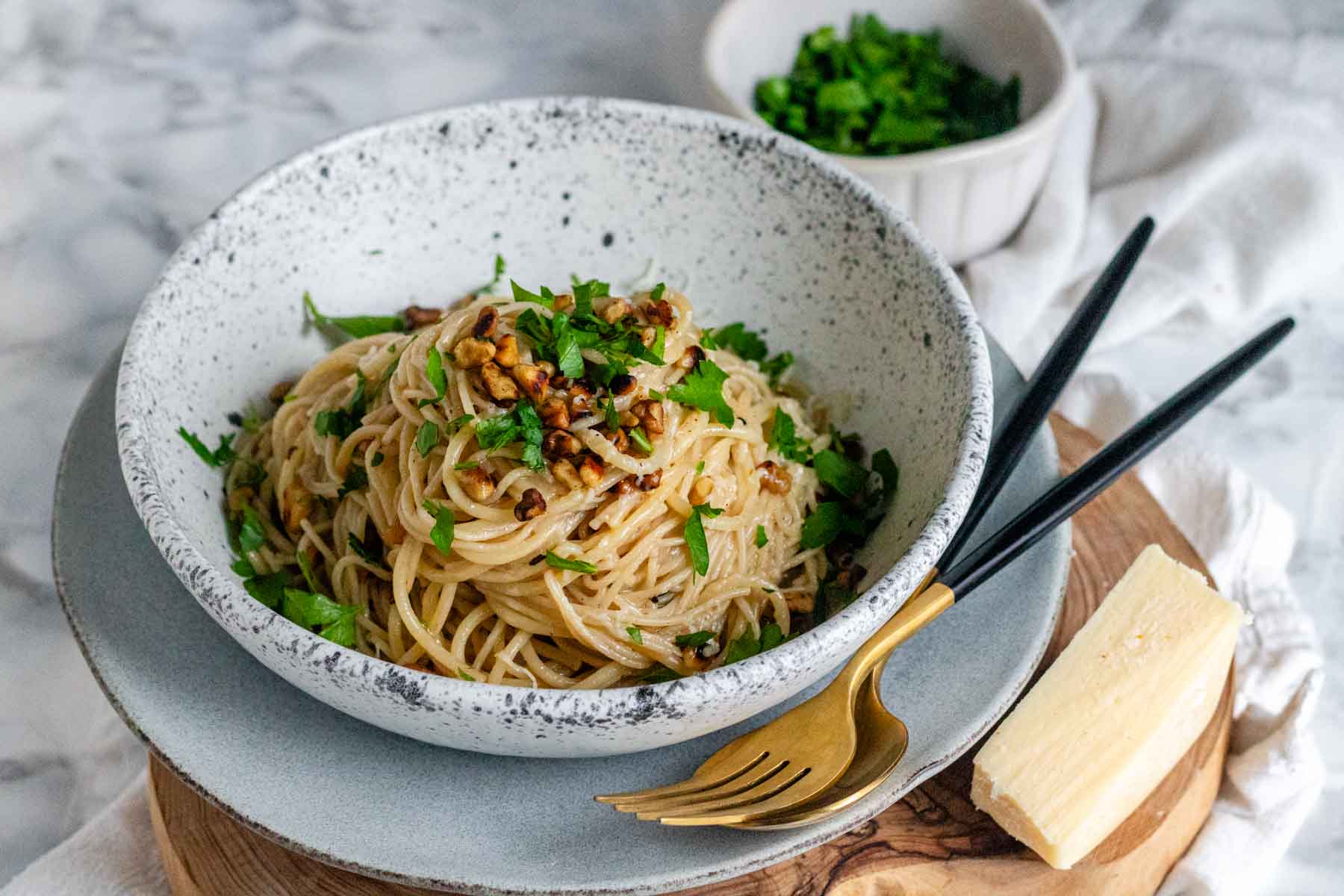 Pasta with brown butter, walnuts, and parsley in a white and black speckled bowl.