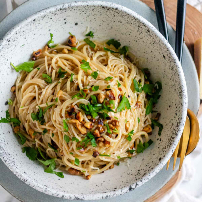 Pasta with brown butter, walnuts, and parsley in a white and black speckled bowl.